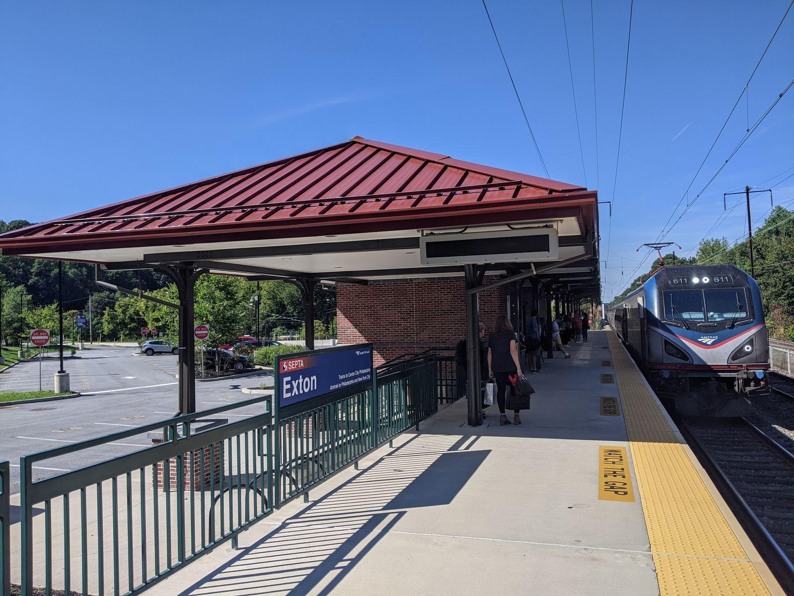 An Amtrak Keystone train arriving at the Exton station platform under a red-roofed shelter