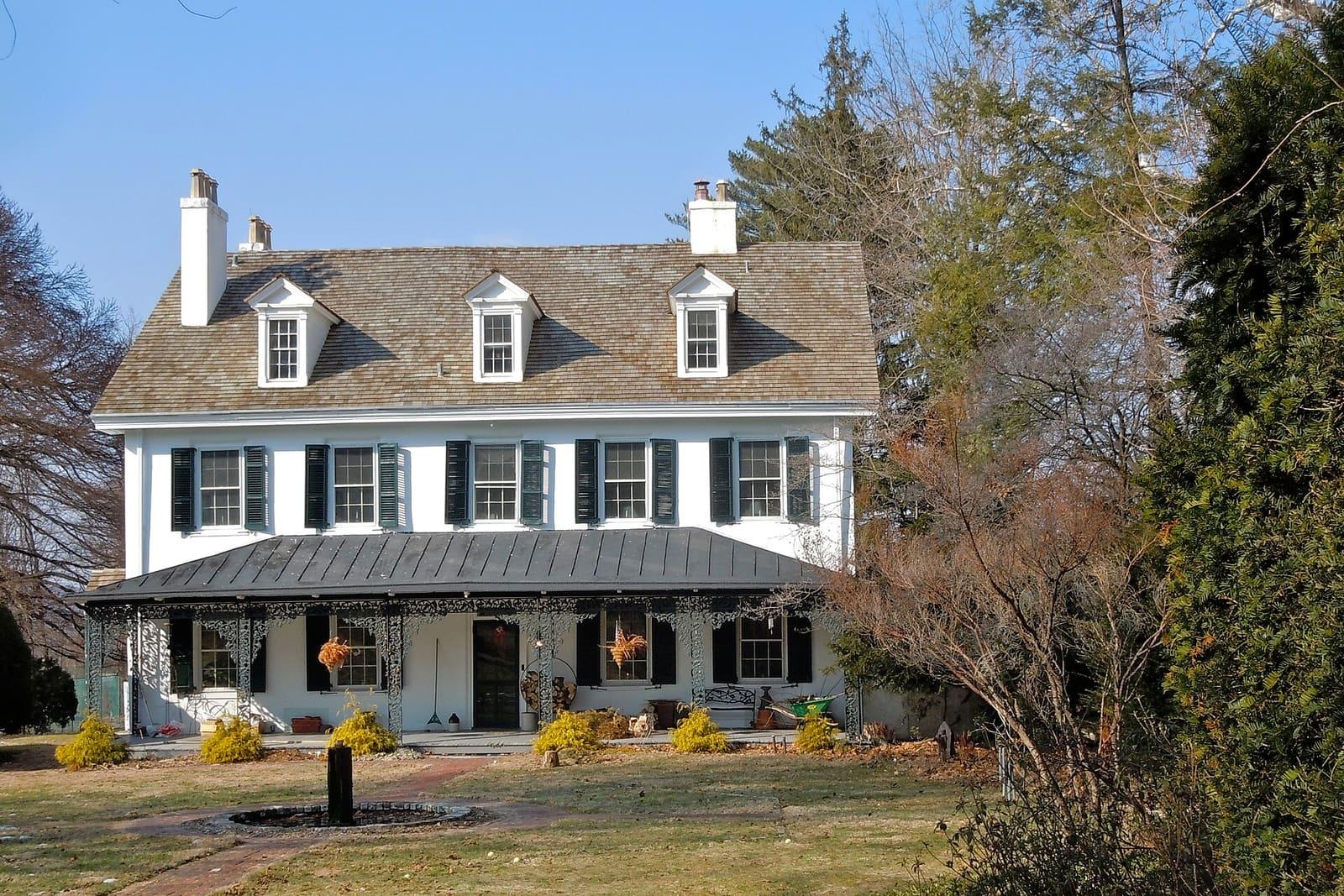 White colonial farmhouse with dormers and a wide porch near Wayne
