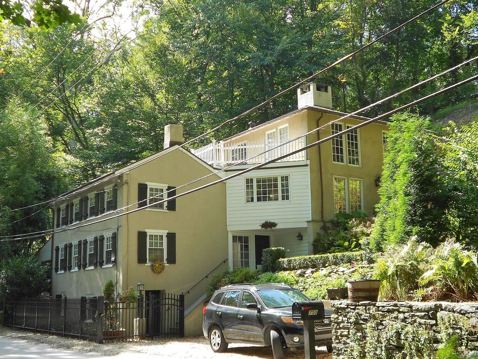 Two joined historic houses with dark shutters on a wooded hillside on Mill Creek Road, in the Mill Creek Historic District near Gladwyne