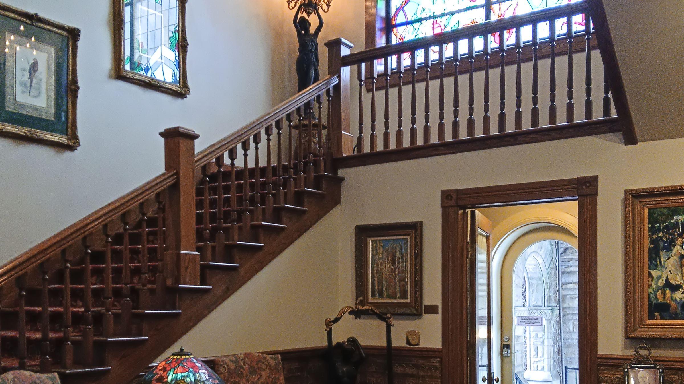 A carved wood grand staircase beneath an arched stained-glass window